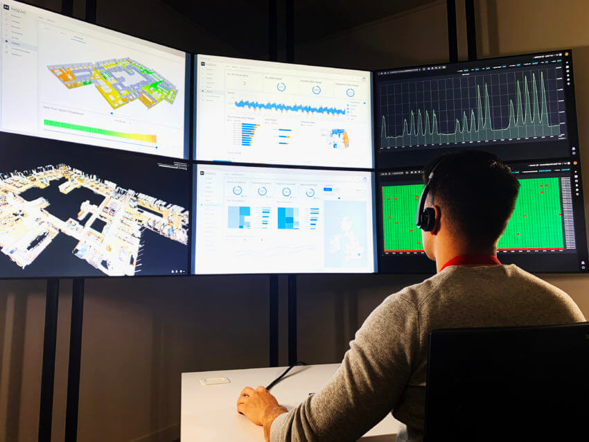 Man sitting in front of several laptop screens, showing various graphs and maps