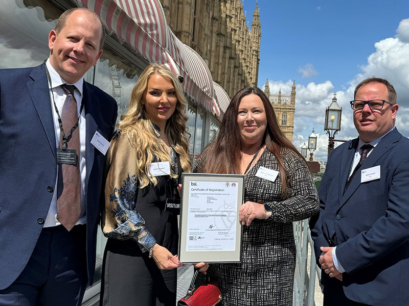 Four Mitie employees holding the BSI Certificate of Registration for ISO 44001, with the London Houses of Parliament in the background