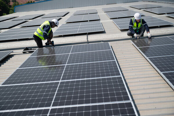 Engineers wearing high vis and hard hats working on solar panels fixed to a roof