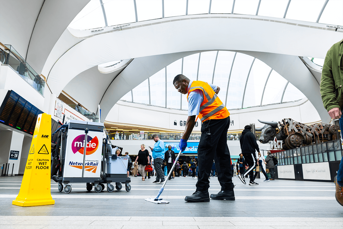 Mitie cleaner sweeping a floor in a busy railway station