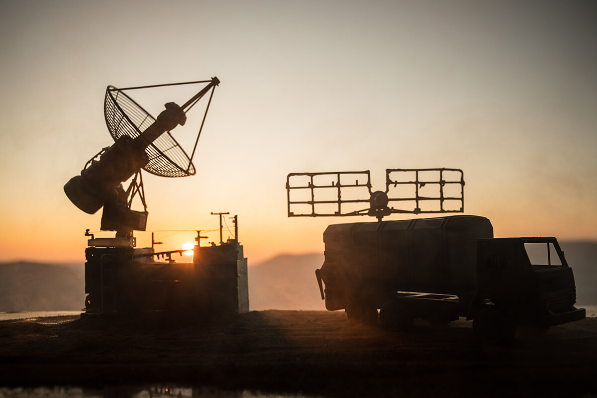 Silhouette of mobile air defence truck with radar antenna during sunset. Satellite dishes or radio antennas against evening sky.
