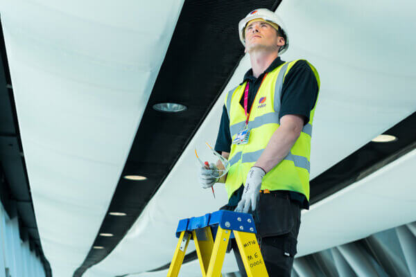 Mitie male engineer fixing a light while standing on a ladder