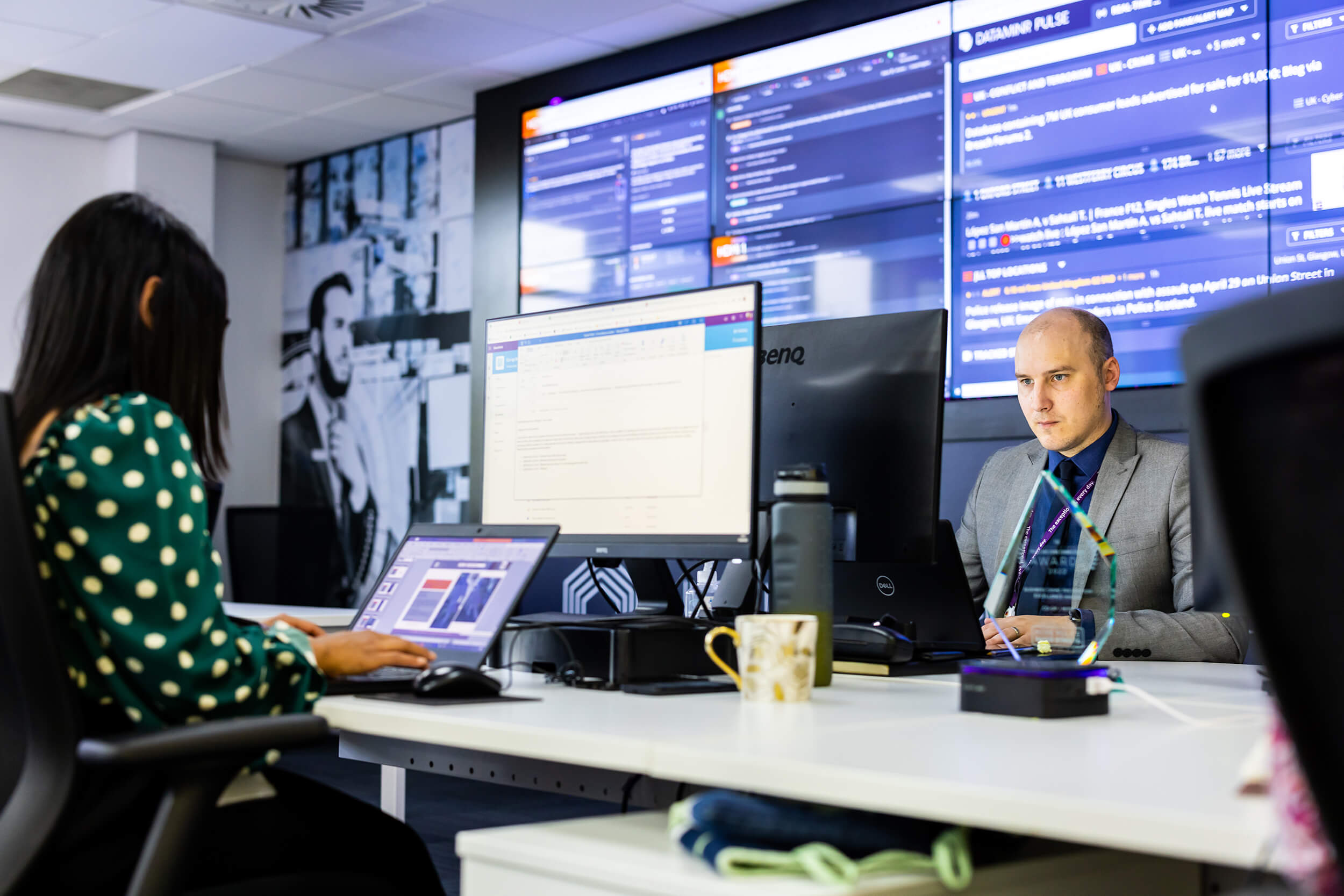 Desk staff using computers for Mitie Intelligence, with screens on the walls